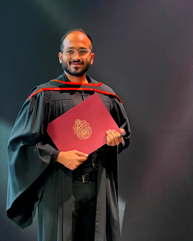 Karthikeyan Umesh in graduation robes at Concordia convocation, holding his diploma folder