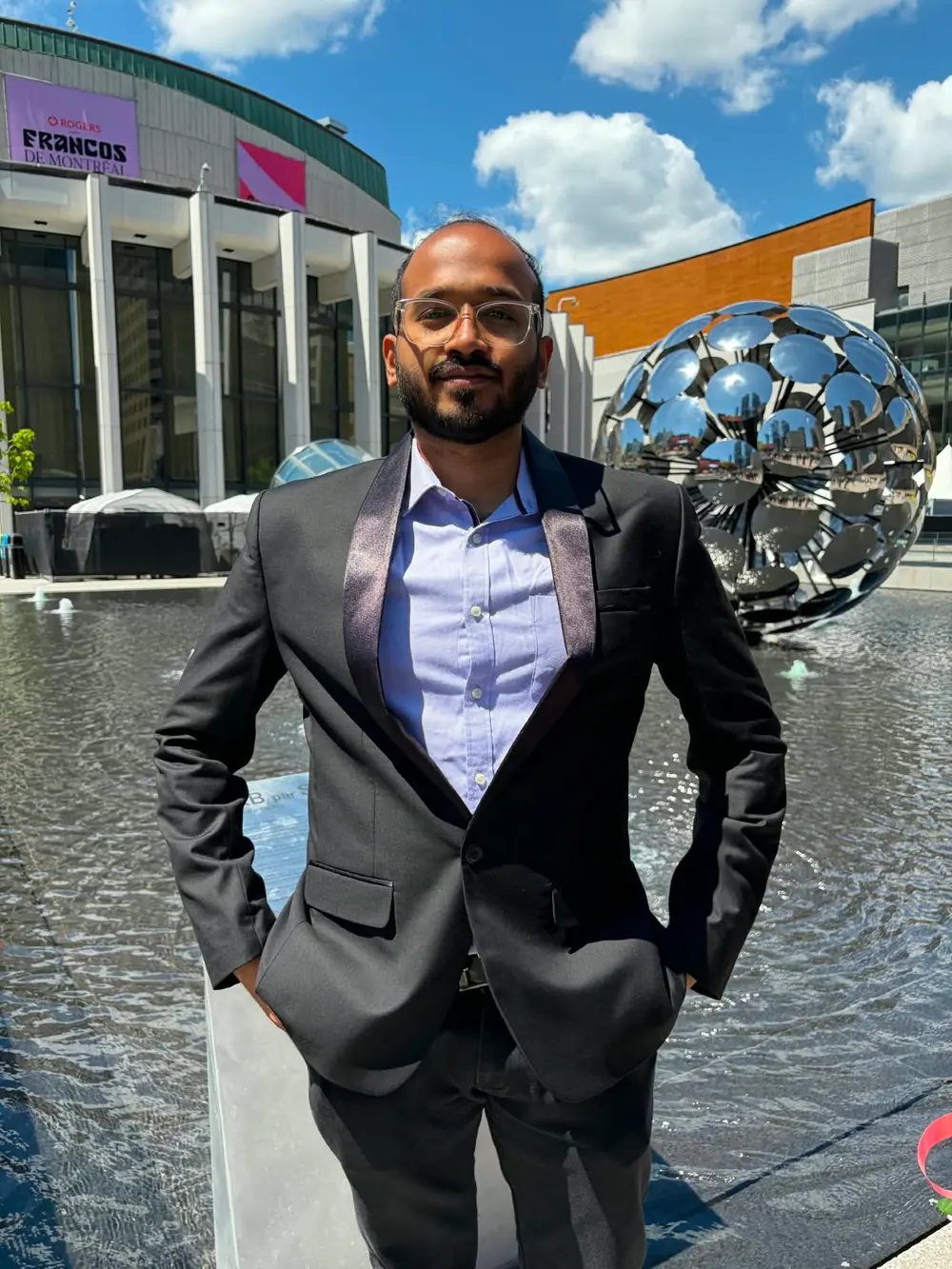 Karthikeyan Umesh in a dark suit at Place des Arts, Montréal, on a sunny day