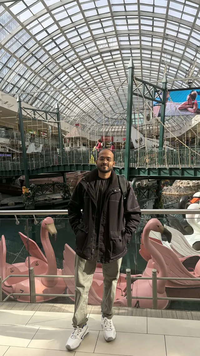 Karthik under the glass roof of West Edmonton Mall, with pink swan boats behind him