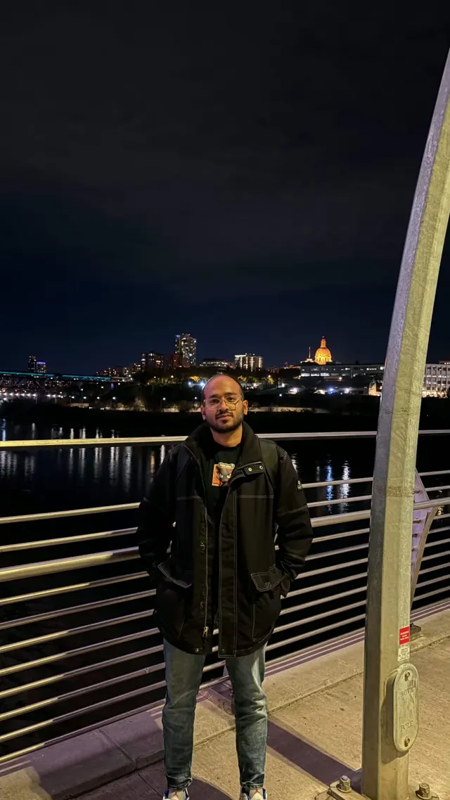 Karthik on a bridge at night with the Edmonton skyline and the lit Alberta Legislature dome behind him
